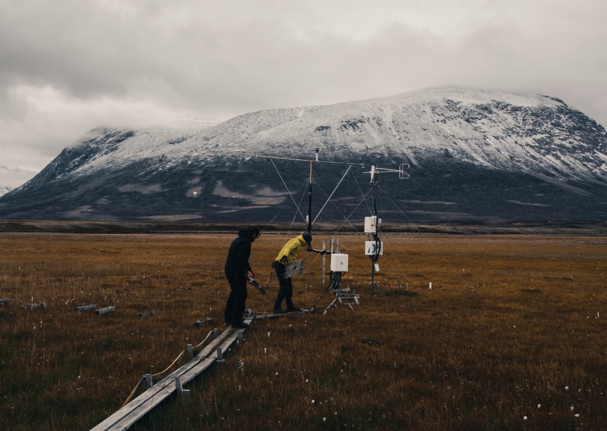 Scientists working around a measurement tower with a snow covered mountain in the background