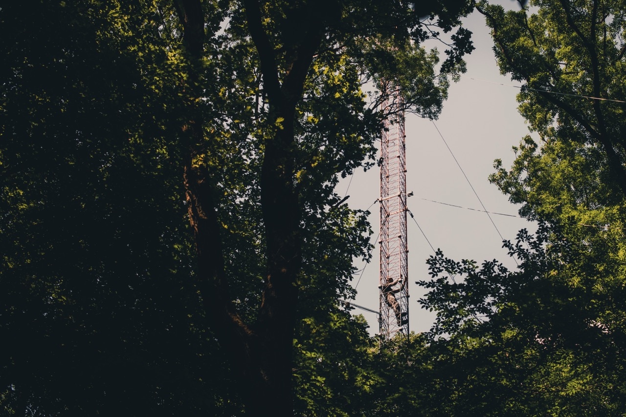 man climbing up a measurement tower in a green forest